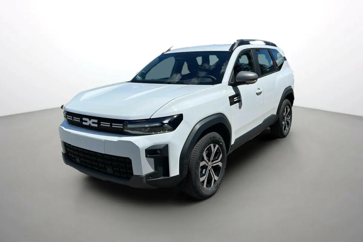 Vue 3/4 avant d'un Dacia Bigster blanc glacier avec barres de toit et jantes alu 17 pouces sur fond neutre.