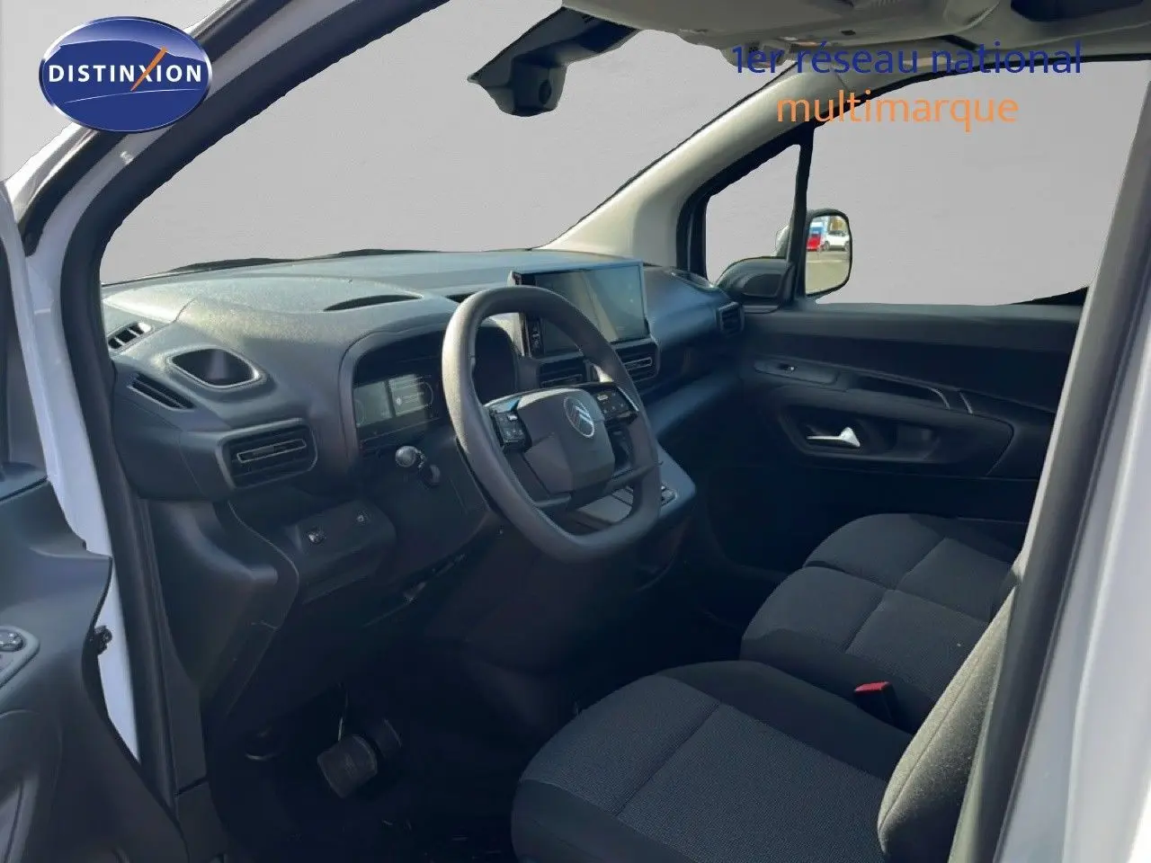 Vue intérieure côté conducteur du Citroën Berlingo blanc icy 2025, montrant le tableau de bord et les sièges tissu noirs.