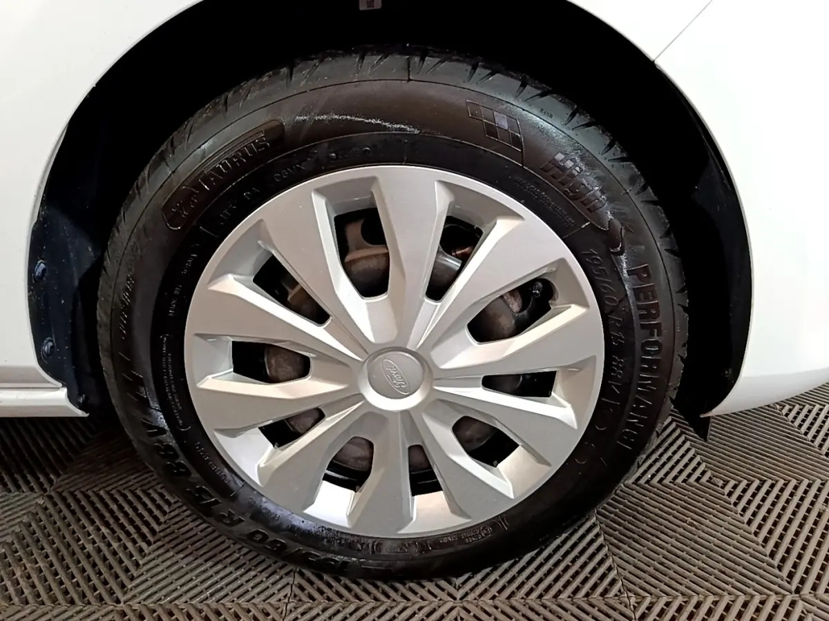 Gros plan sur la roue avant gauche d'une Ford Fiesta blanche, mettant en valeur la jante et le pneu noir.