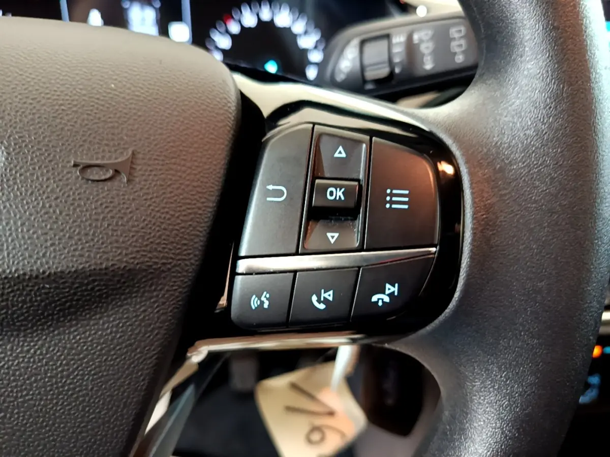 Gros plan sur les commandes multifonctions au volant noir d'une Ford Fiesta blanche, avec boutons de navigation et appel.