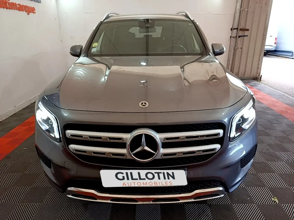 Vue avant d’un Mercedes GLB 200 d Business Line gris foncé avec calandre chromée et phares LED allumés.