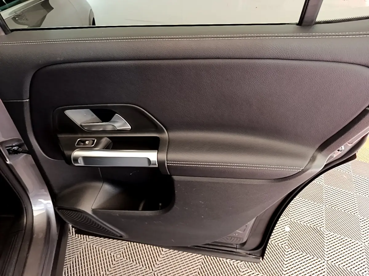 Vue intérieure de la porte arrière gauche du Mercedes GLB 200 d Business Line gris foncé, avec poignée argentée et commande de fenêtre.