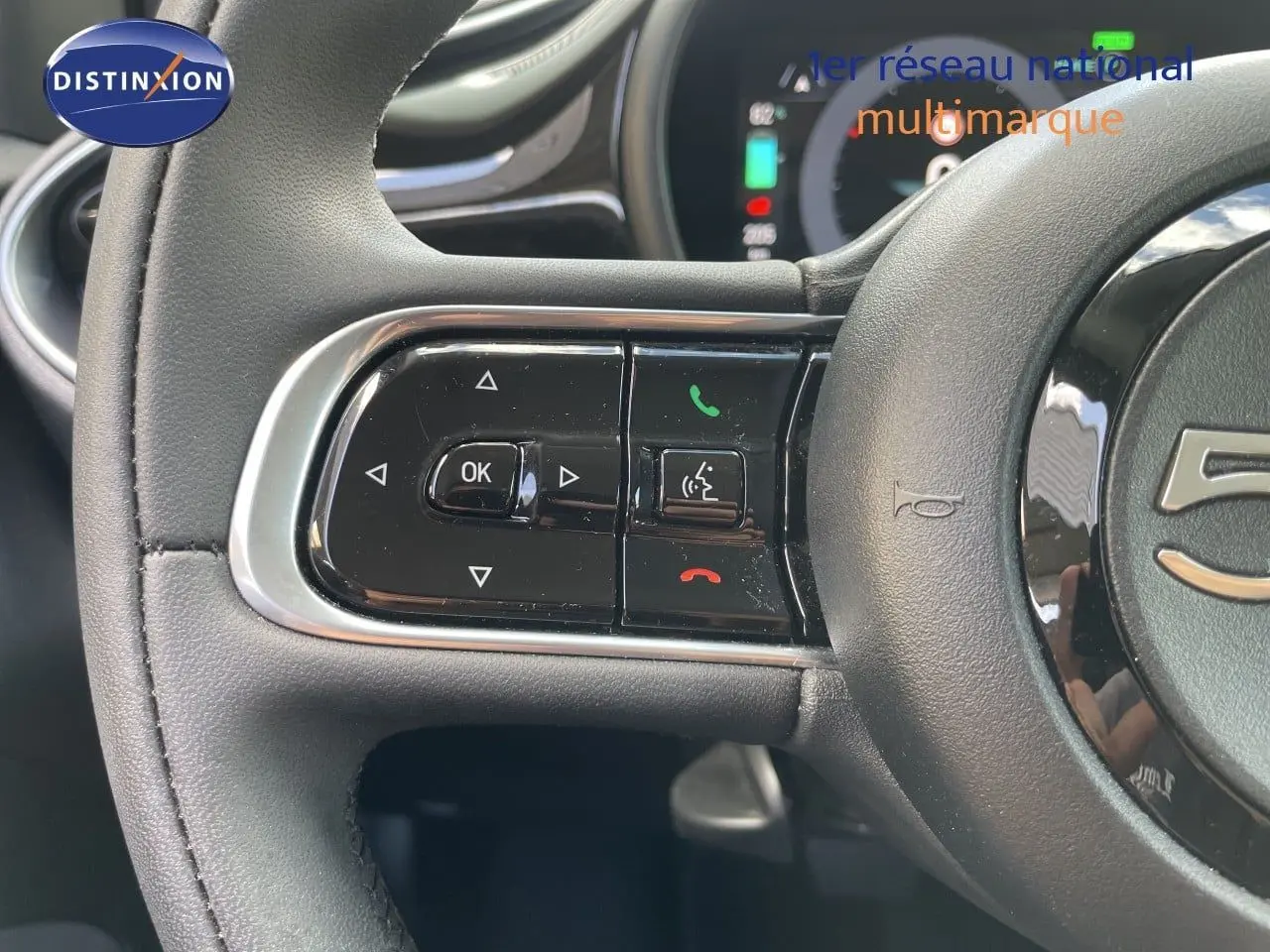 Gros plan sur les commandes gauche du volant noir de la Fiat 500 électrique 2023, avec boutons multifonctions et finition brillante.