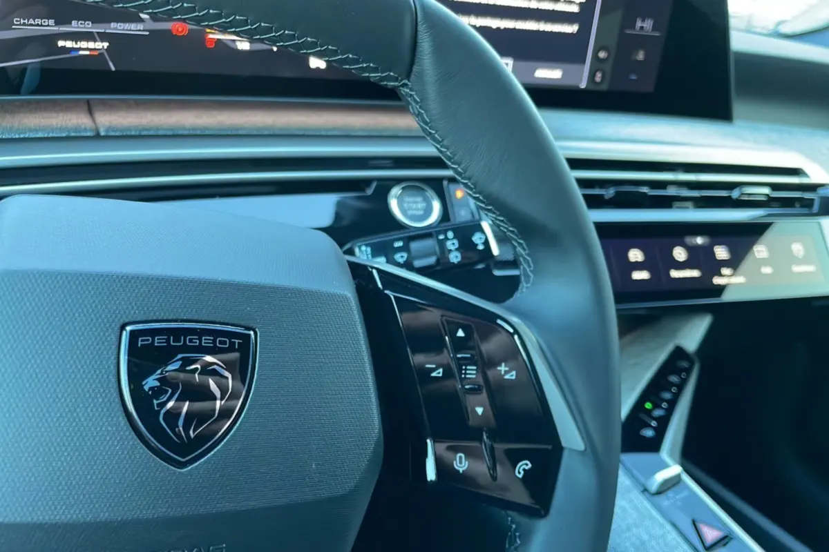 Gros plan sur le volant cuir noir du Peugeot 5008 Hybrid 145 Allure Plus 2025 avec commandes intégrées et tableau de bord digital.