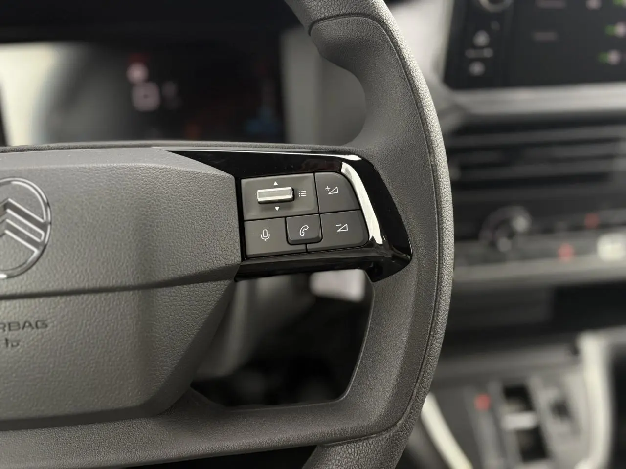 Gros plan sur les commandes audio et vocales du volant du Citroën Jumpy 2025, intérieur gris et noir flouté en arrière-plan