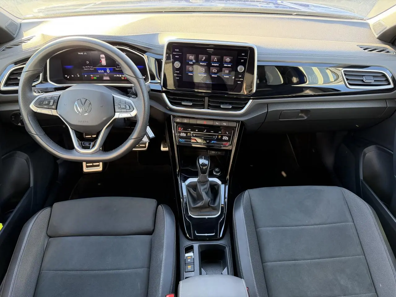 Vue intérieure frontale du tableau de bord et volant Volkswagen T-Roc 2025, finition R-Line avec écran tactile et sellerie noire.