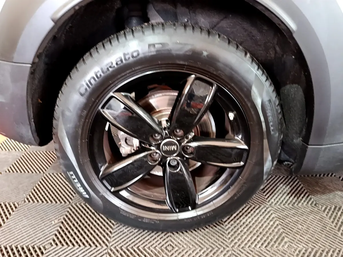 Gros plan sur la roue avant droite du MINI Countryman gris clair, jante noire brillante à cinq branches.