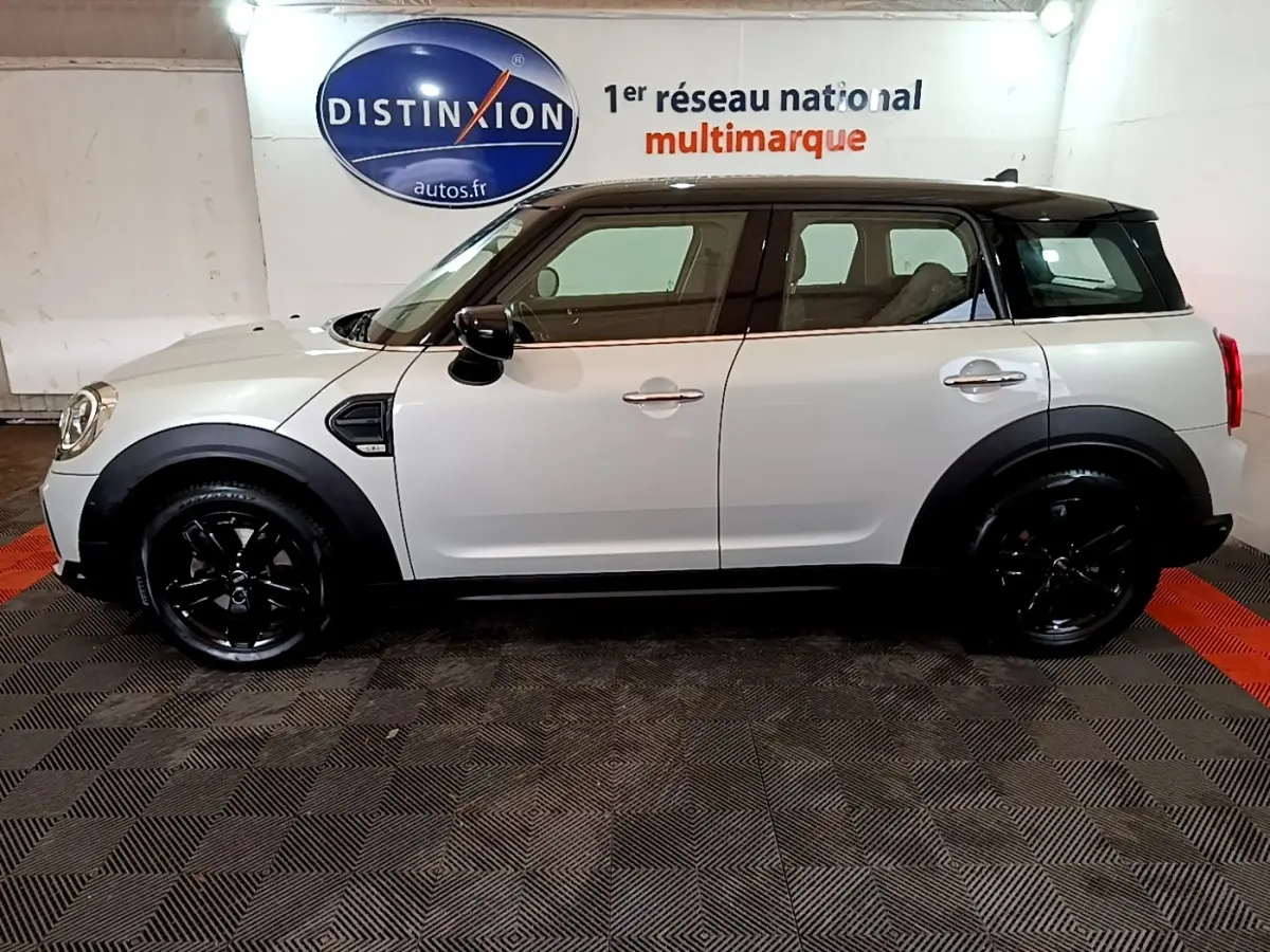 Vue de profil côté gauche d'une MINI Countryman gris clair avec toit et jantes noires dans un showroom.