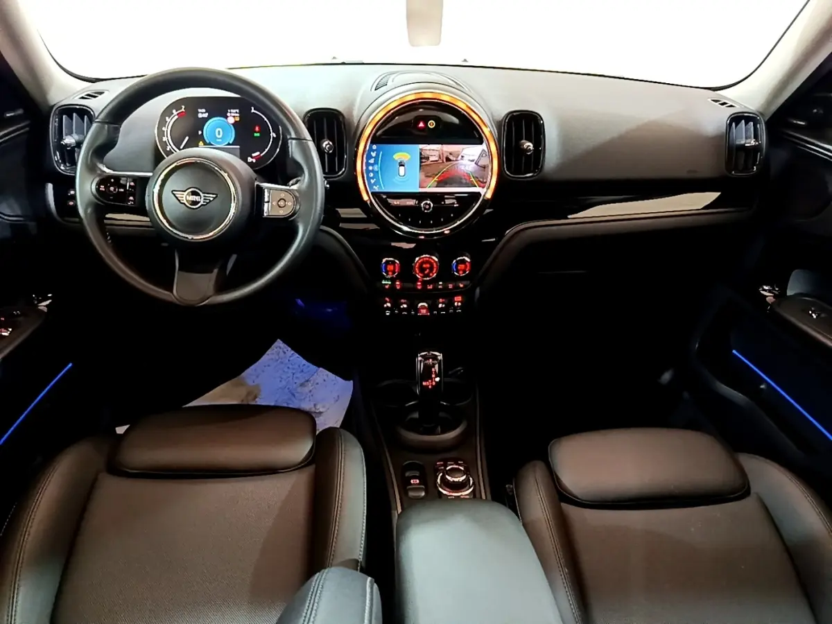 Vue intérieure avant du tableau de bord noir et volant cuir d'une MINI Countryman gris clair avec éclairage d'ambiance bleu.