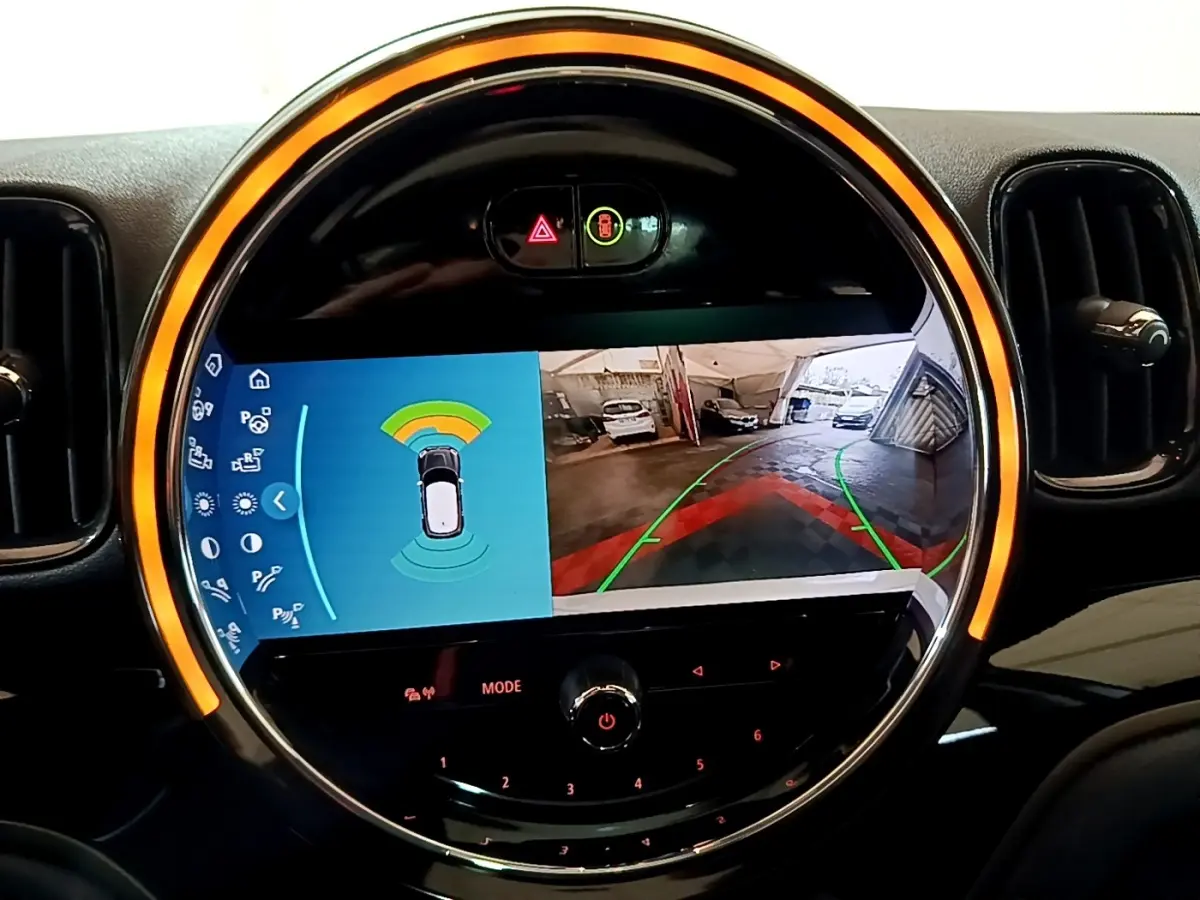 Vue rapprochée de l’écran tactile central rond avec affichage de l’aide au stationnement du MINI Countryman gris clair.