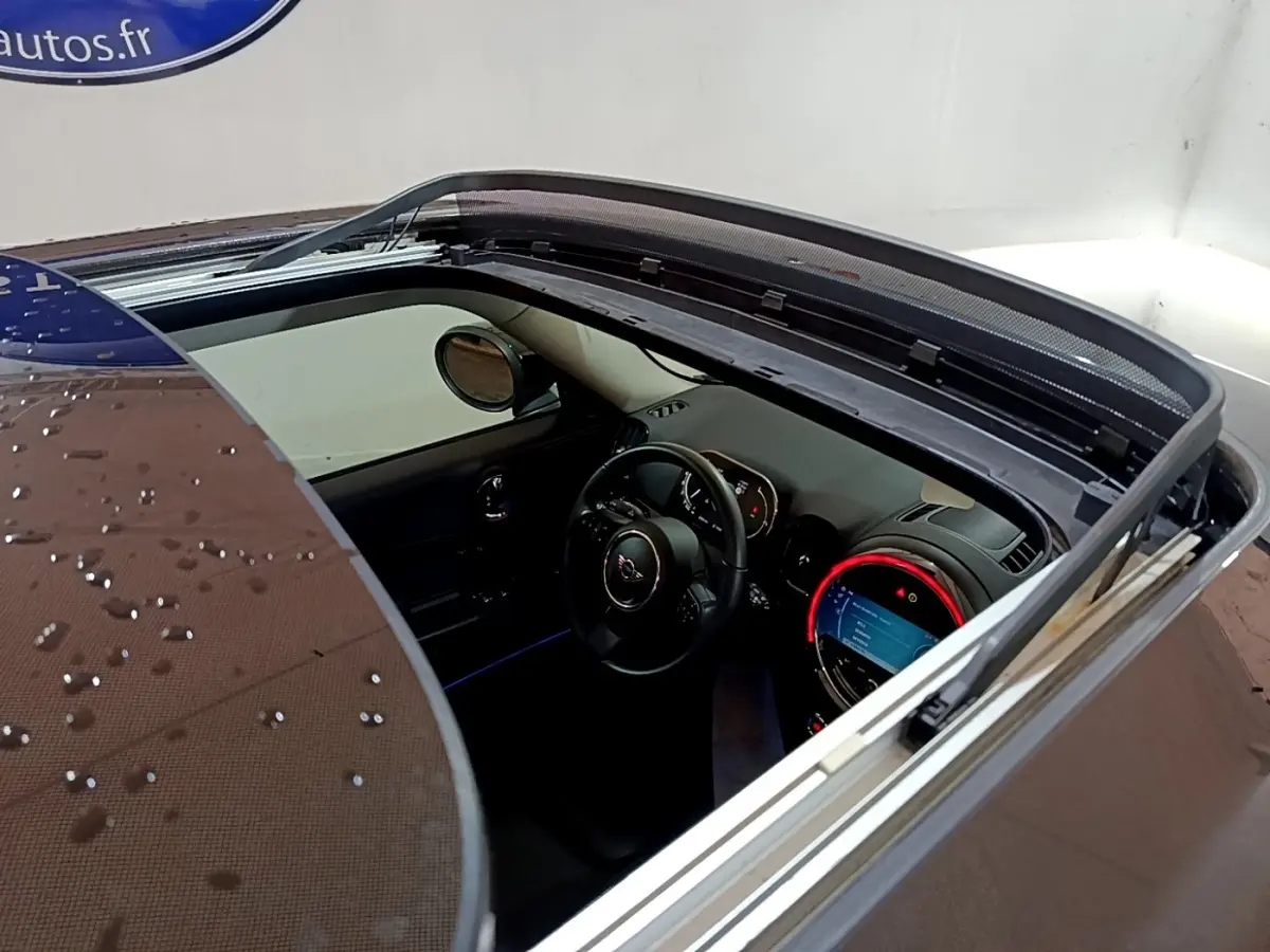 Vue plongeante sur l'intérieur d'une MINI Countryman gris clair avec toit ouvrant électrique et tableau de bord éclairé.