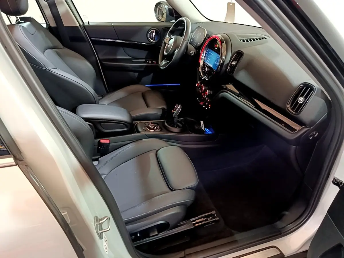 Vue intérieure côté conducteur de la MINI Countryman gris clair 2022, sièges cuir noirs et tableau de bord lumineux.