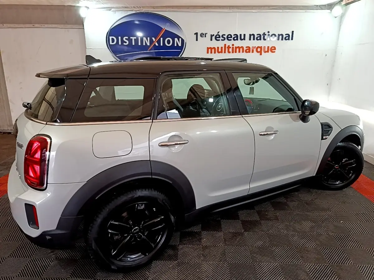 Vue côté droit arrière d'une MINI Countryman gris clair avec toit noir et jantes noires brillantes en intérieur showroom.