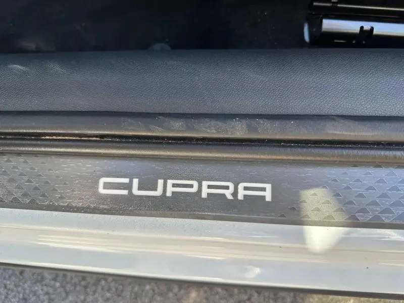 Gros plan sur la plaque de seuil de porte avec le logo CUPRA, sur un véhicule blanc Nevada métallisé.