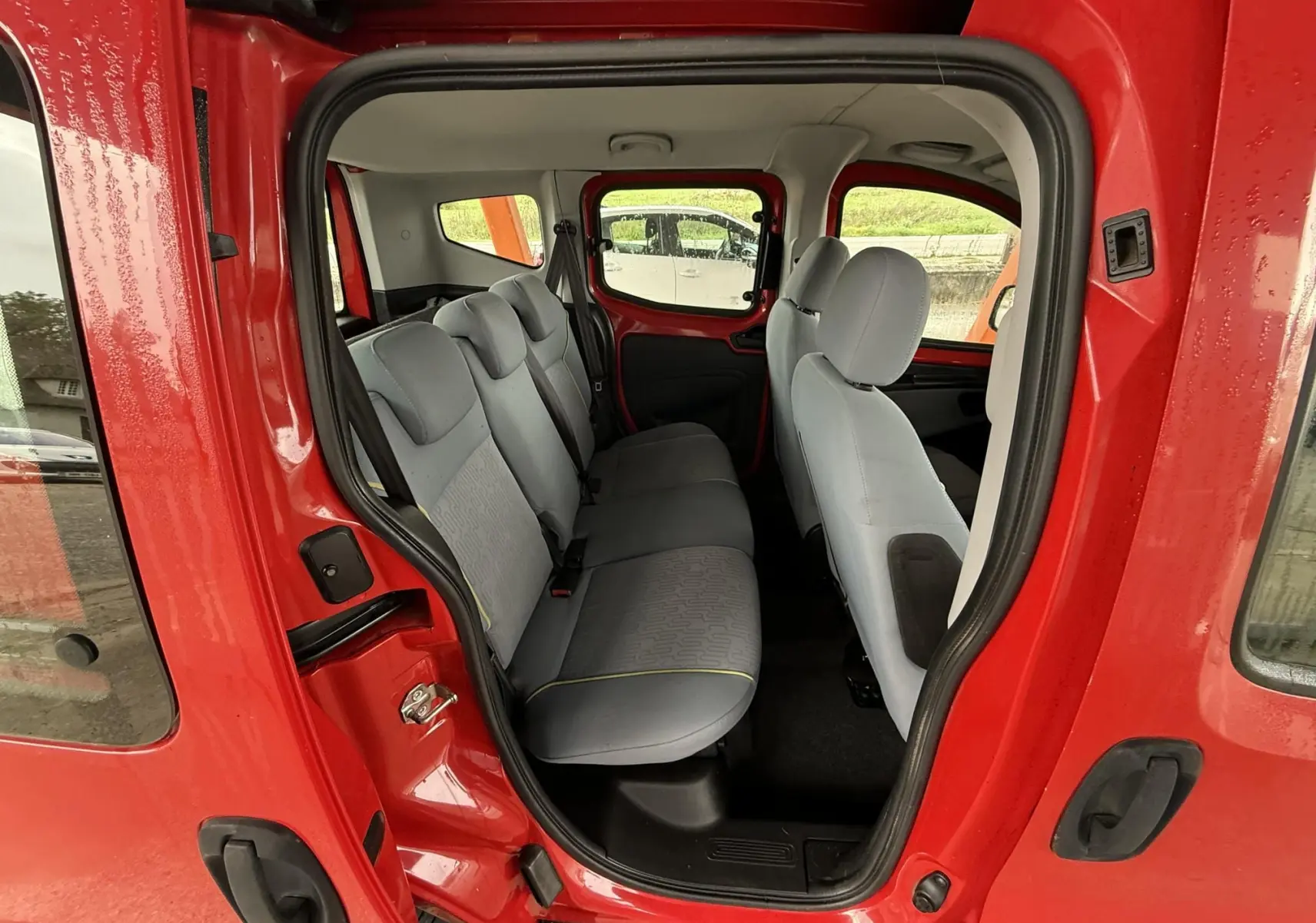 Vue intérieure côté droit du Peugeot Bipper Tepee rouge, montrant la banquette arrière en tissu gris et la porte coulissante ouverte.