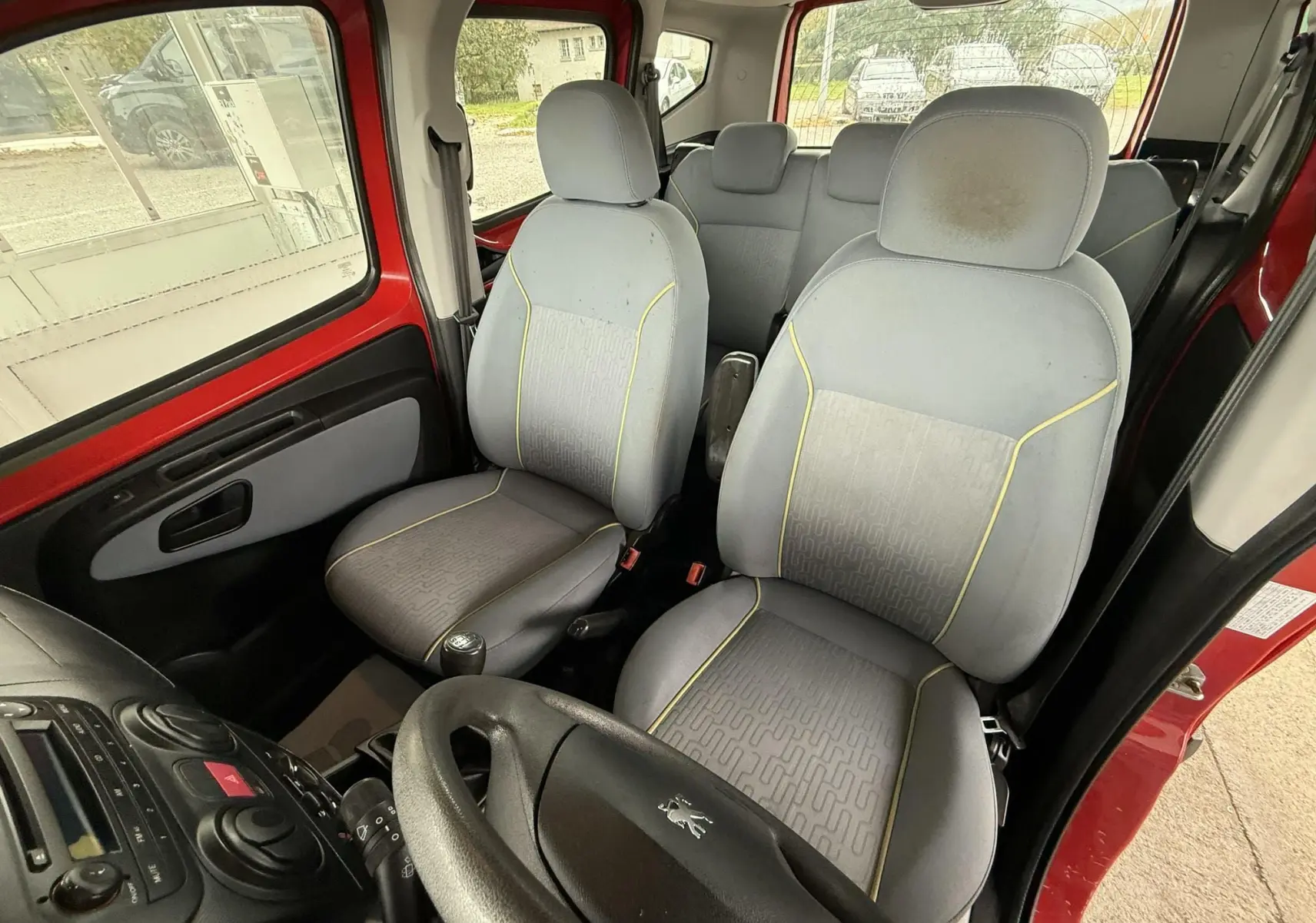 Intérieur du Peugeot Bipper Tepee rouge, vue côté conducteur montrant sièges tissu gris et volant Peugeot.