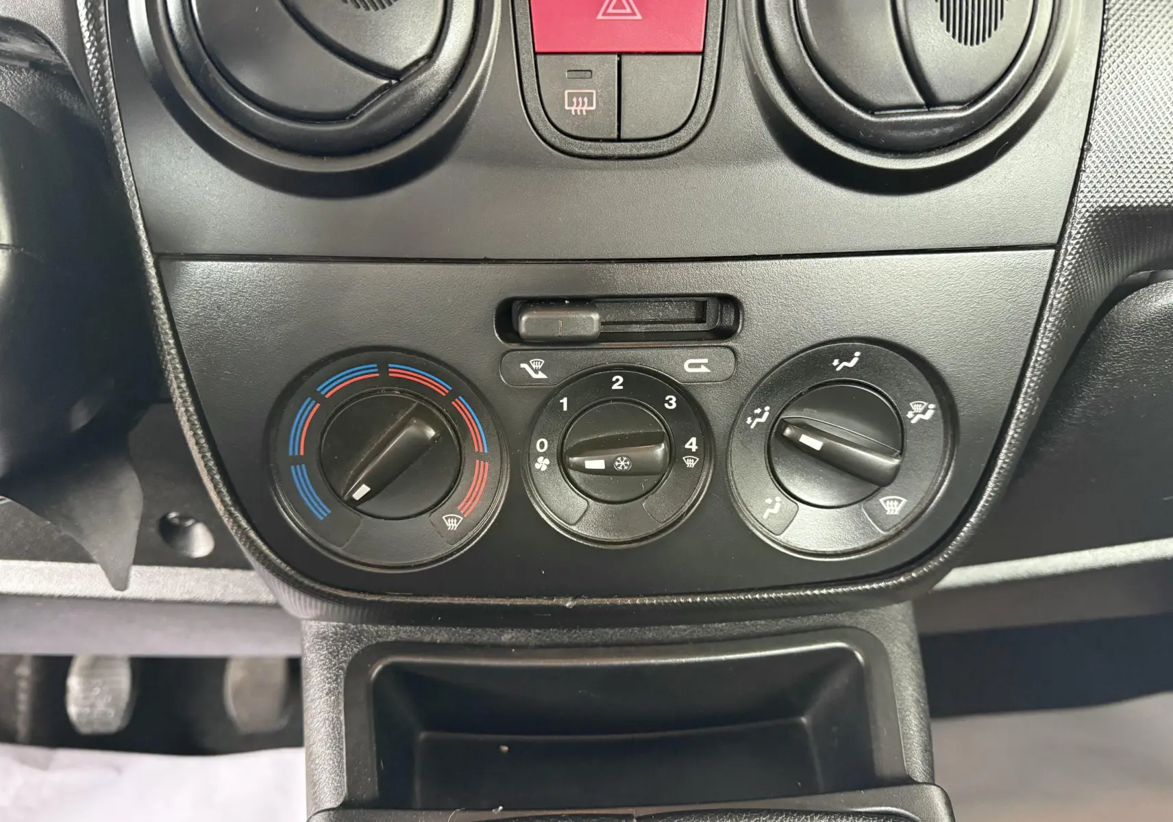 Gros plan sur les commandes de climatisation noires du tableau de bord d'un Peugeot Bipper Tepee rouge, version 2013.