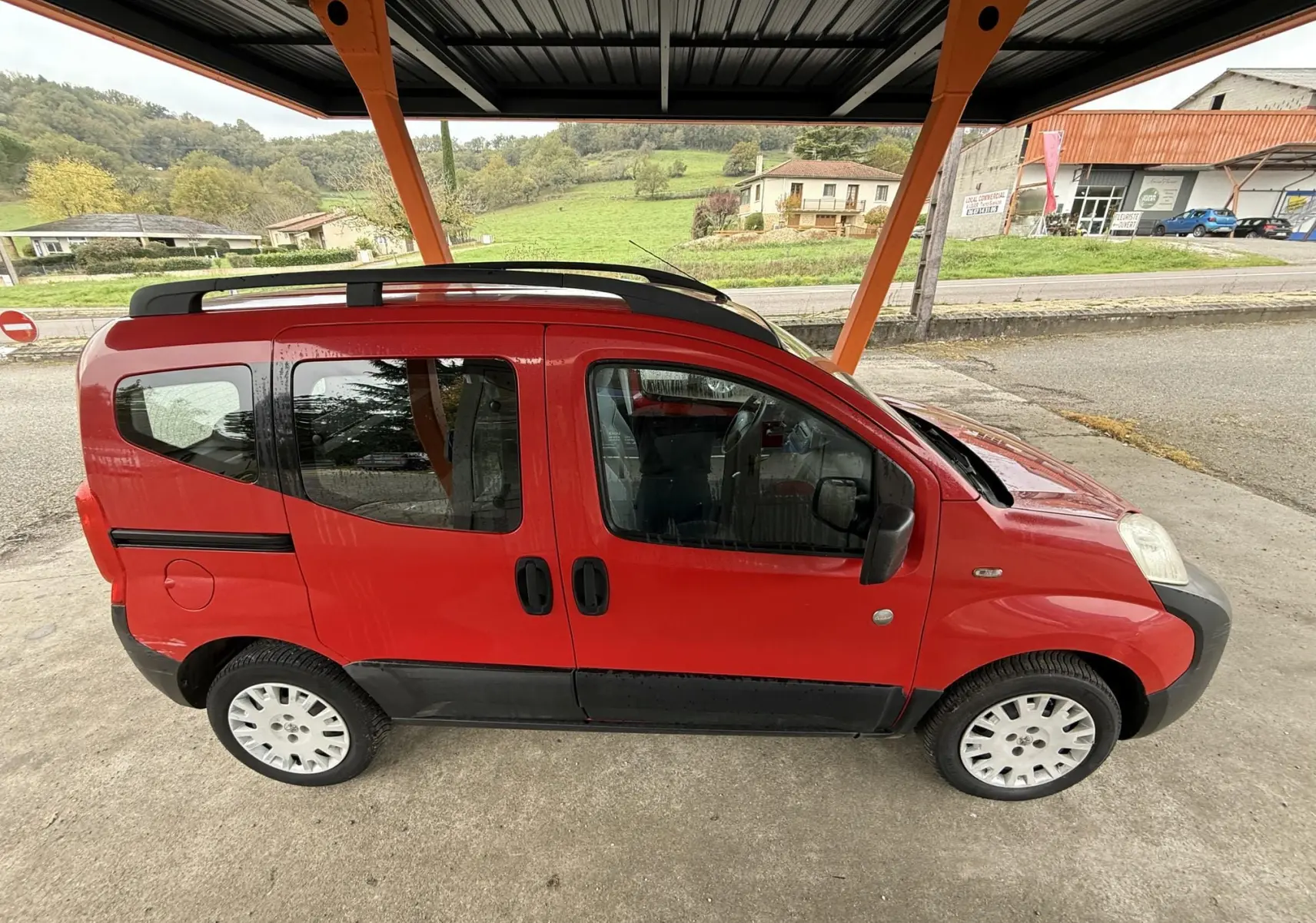 Profil droit du Peugeot Bipper Tepee rouge, avec portes coulissantes et jantes 15 pouces sous abri.