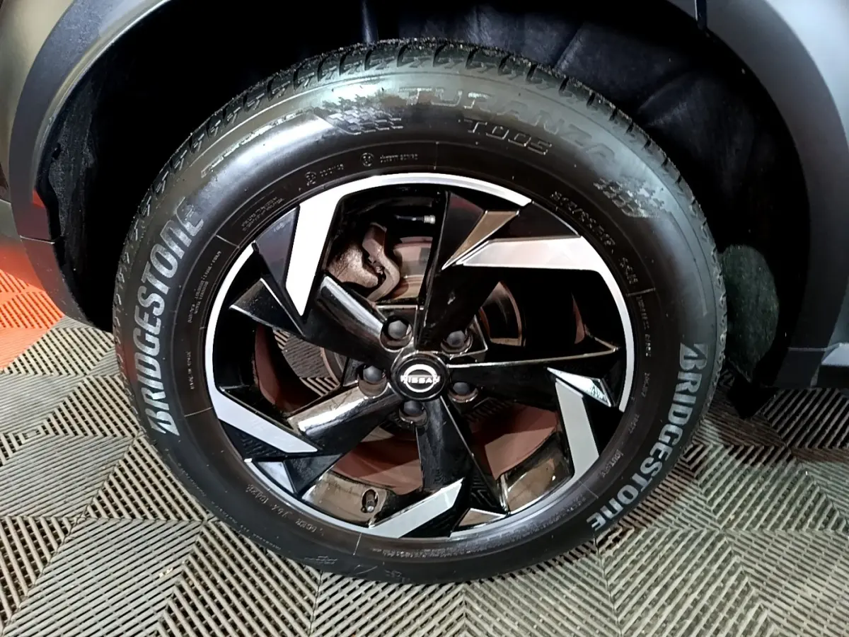 Gros plan sur la roue avant droite du Nissan Juke Hybrid 143 Business+ noire, jante alliage noire et argentée, pneu Bridgestone.