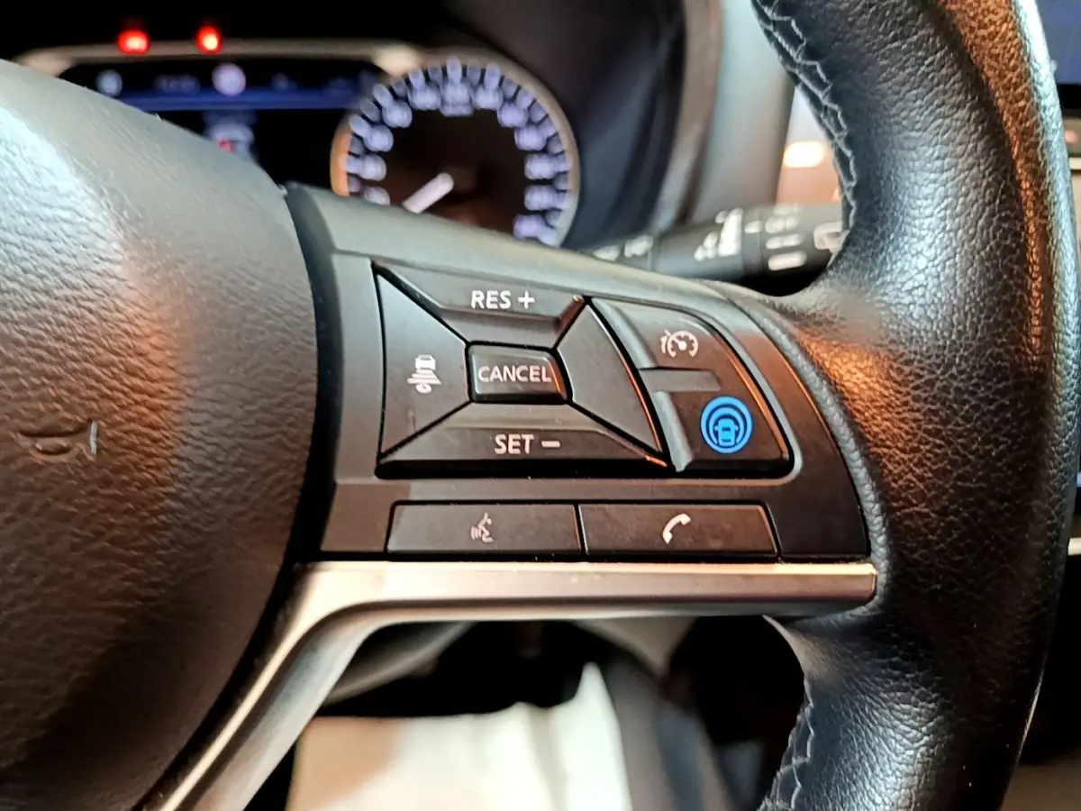 Gros plan sur les commandes à droite du volant en cuir noir du Nissan Juke Hybrid 2022, avec bouton bleu éclairé.