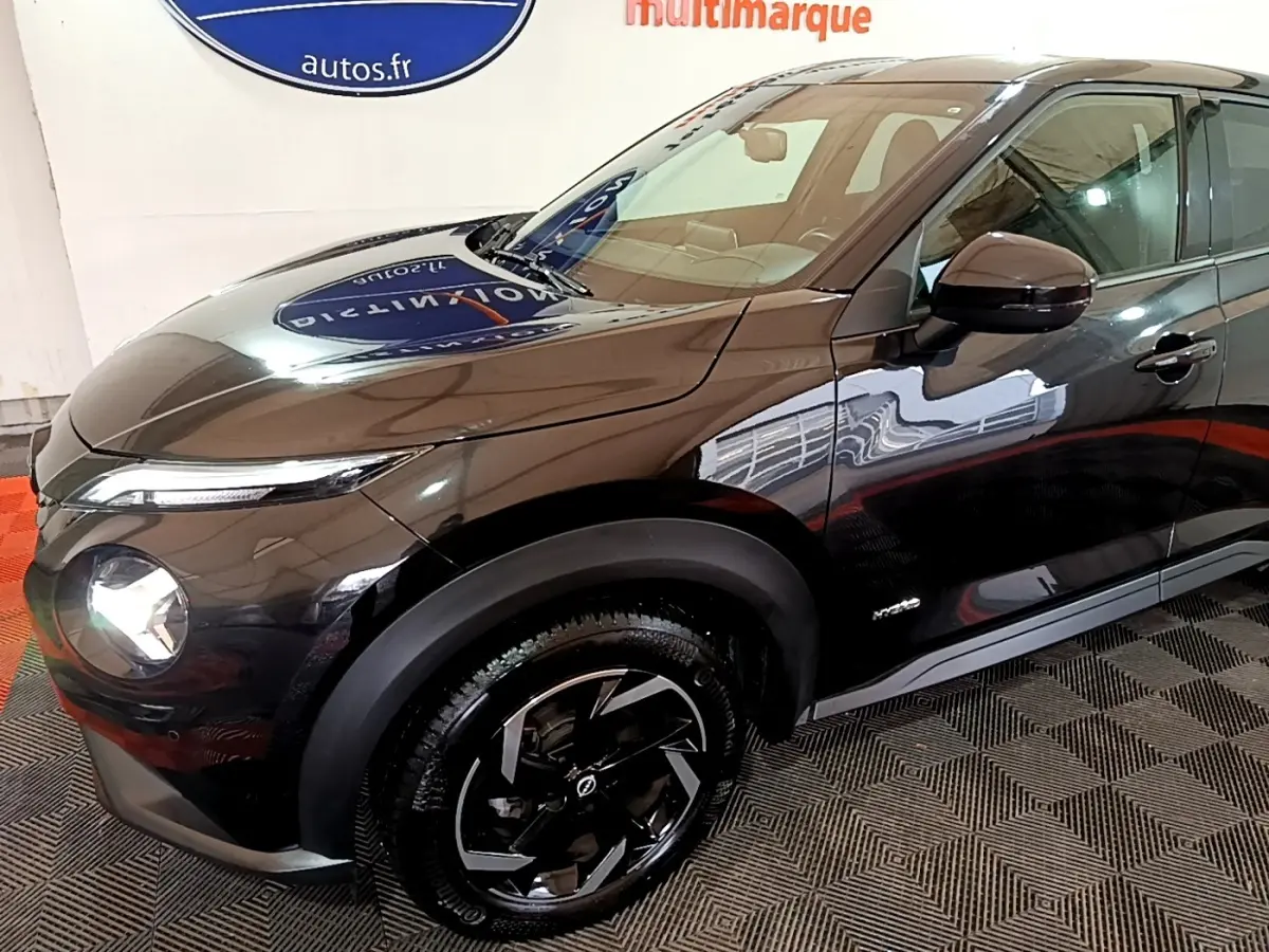 Vue 3/4 avant droit du Nissan Juke Hybrid 143 Business+ noir brillant avec jantes noires et phares allumés.