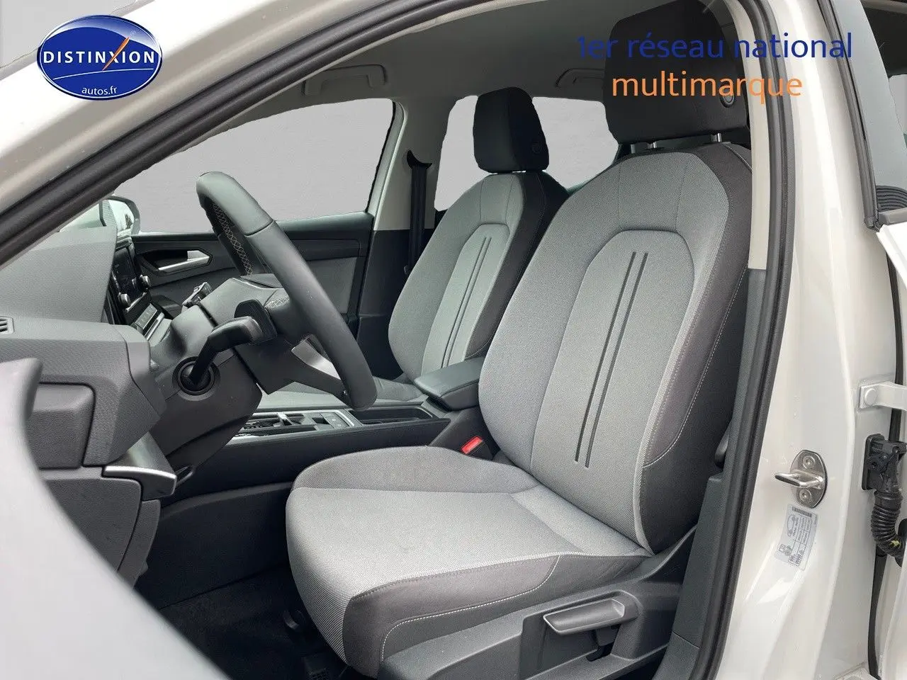 Vue intérieure côté conducteur de la SEAT LEON IV blanche 2024, sièges tissu gris clair avec détails noirs.