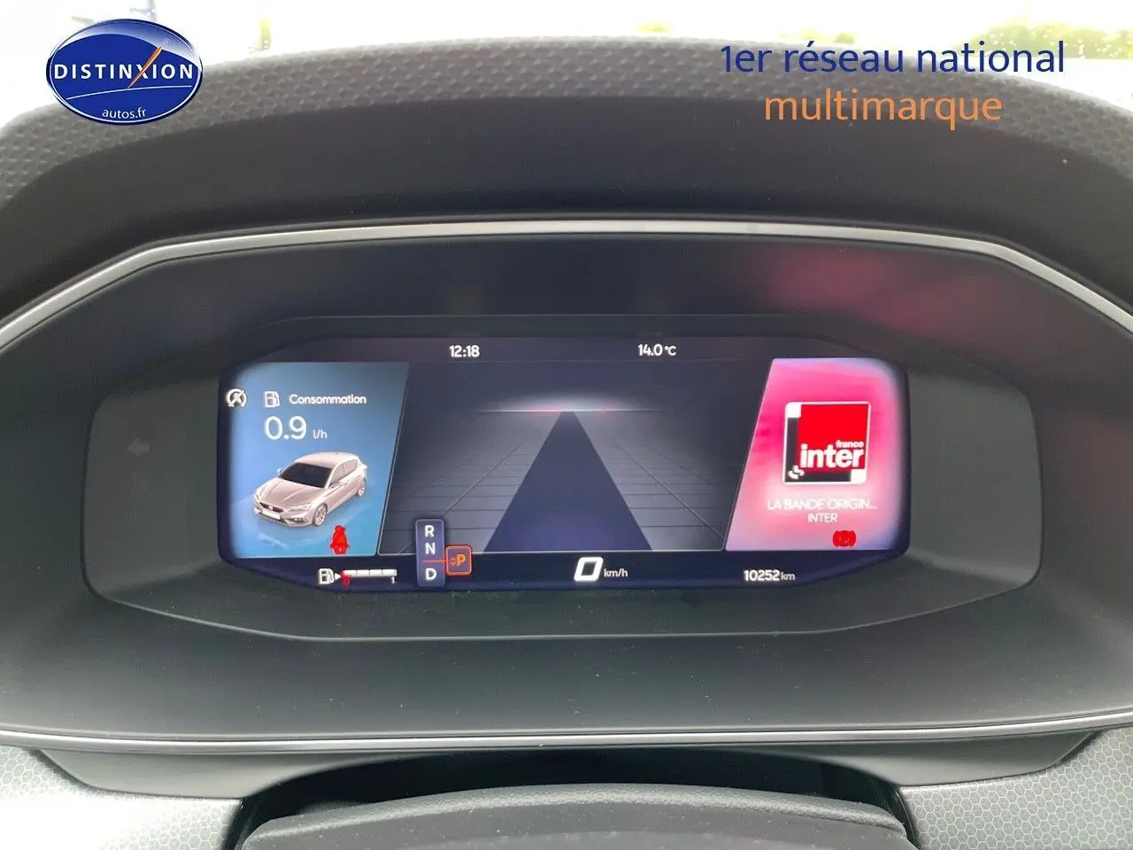 Tableau de bord numérique de la SEAT LEON IV blanc, affichant consommation, vitesse et radio en vue frontale.