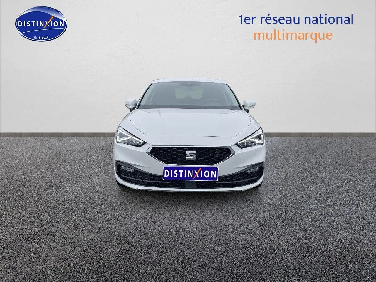 Vue frontale d'une SEAT LEON IV blanche de 2024 avec calandre noire et phares LED allumés.