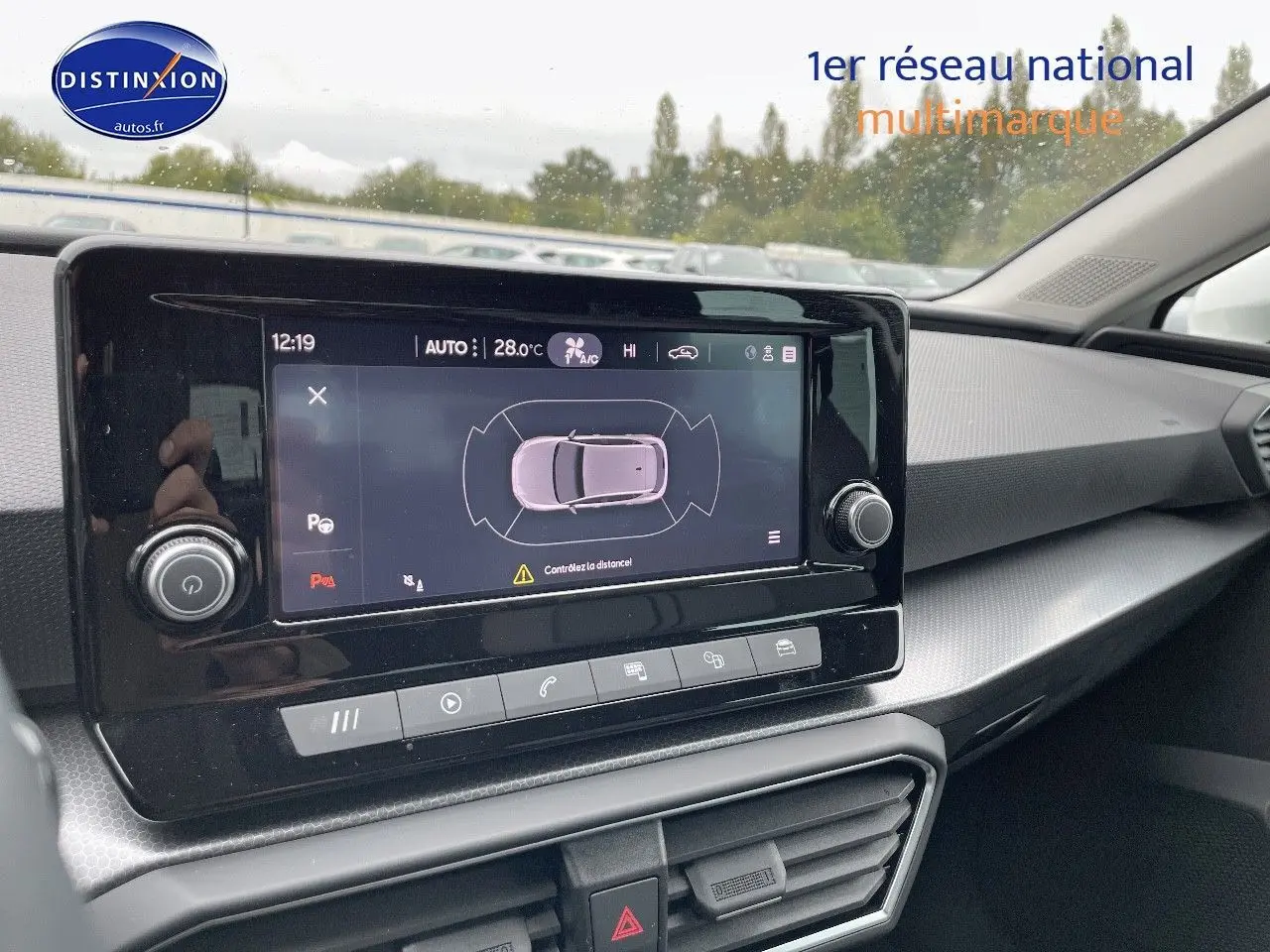 Tableau de bord de la SEAT LEON IV blanche 2024, avec écran tactile affichant l'aide au stationnement et commandes intégrées.