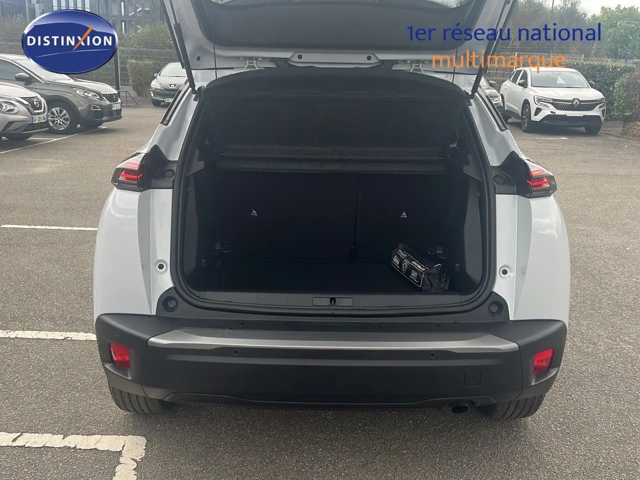 Vue arrière du Peugeot 2008 blanc Okenite Metal 2025 avec coffre ouvert et sac de secours visible à l'intérieur.