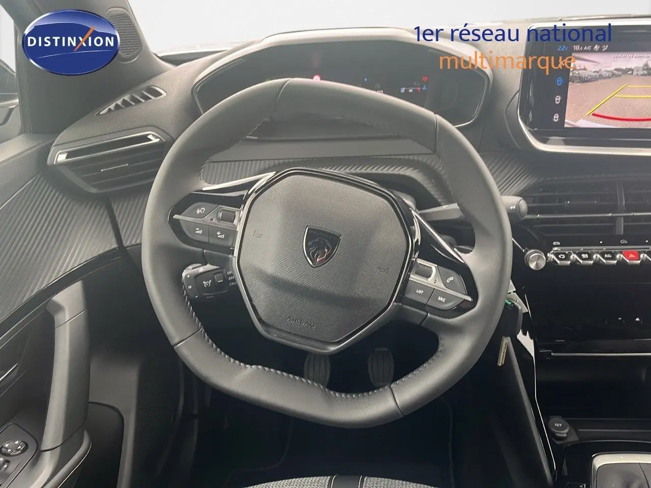 Vue rapprochée du volant cuir noir du Peugeot 2008 blanc Okenite, avec tableau de bord et écran multimédia affichant la caméra de recul.