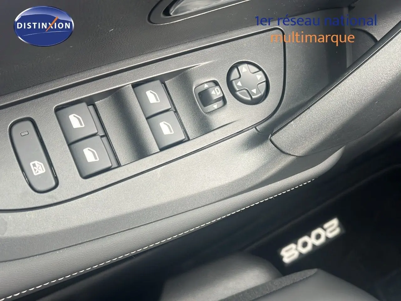 Gros plan sur les commandes de lève-vitres côté conducteur d’un Peugeot 2008 blanc Okenite 2025 avec logo lumineux au sol.