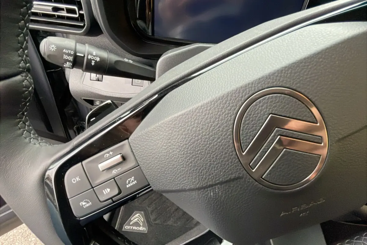 Gros plan sur le volant en cuir du Citroën Berlingo 2025, avec commandes intégrées et logo chromé central.