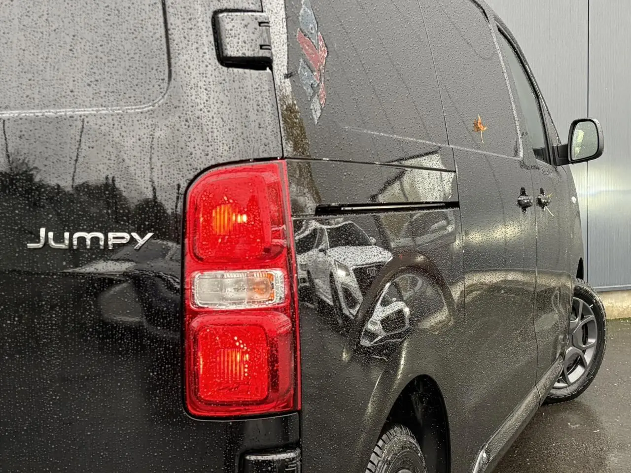 Vue arrière côté droit du Citroën Jumpy noir Perla avec feux arrière allumés sous la pluie.