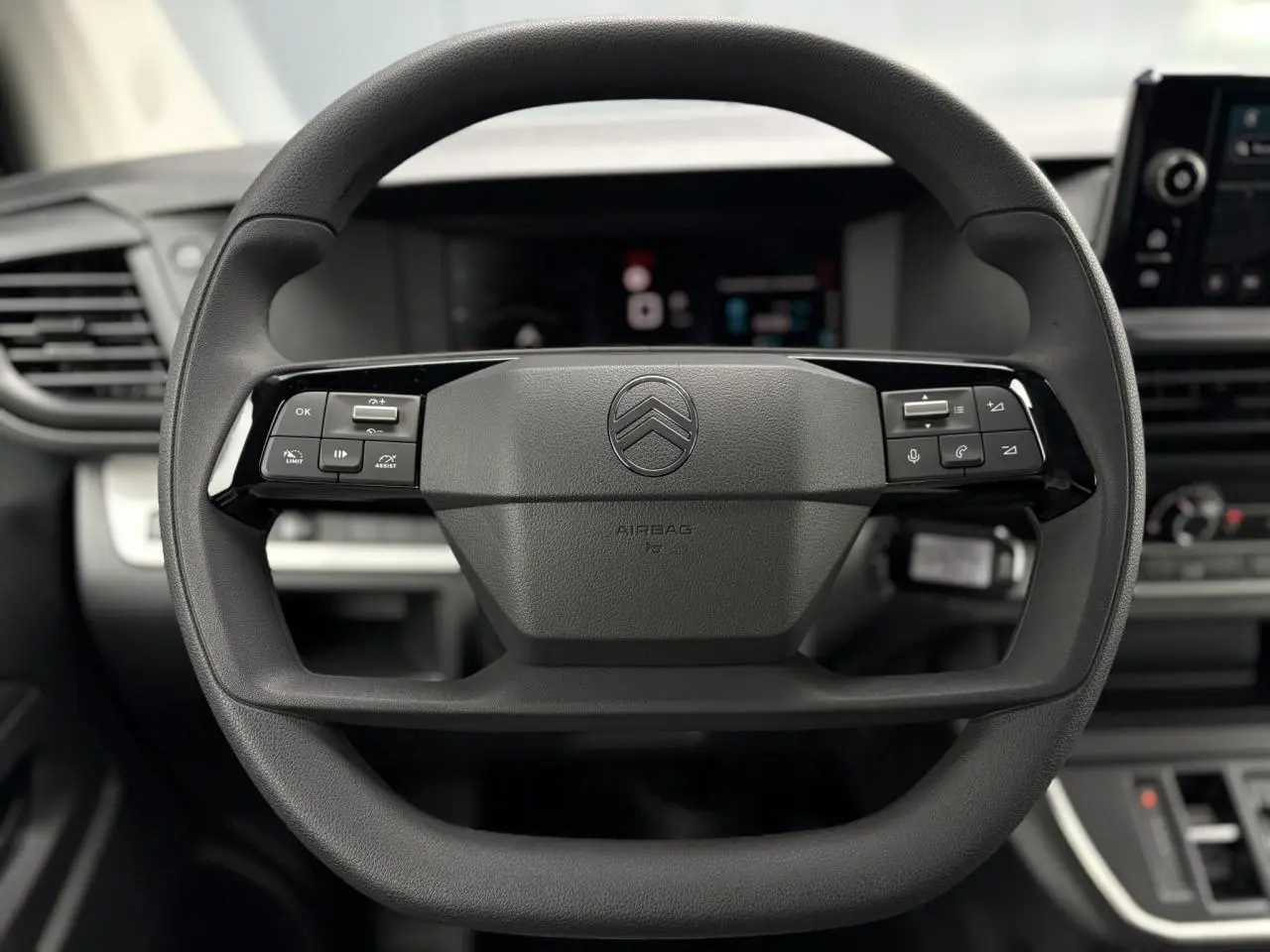 Gros plan sur le volant multifonction noir du Citroën Jumpy 2025 avec commandes intégrées et tableau de bord numérique flou.