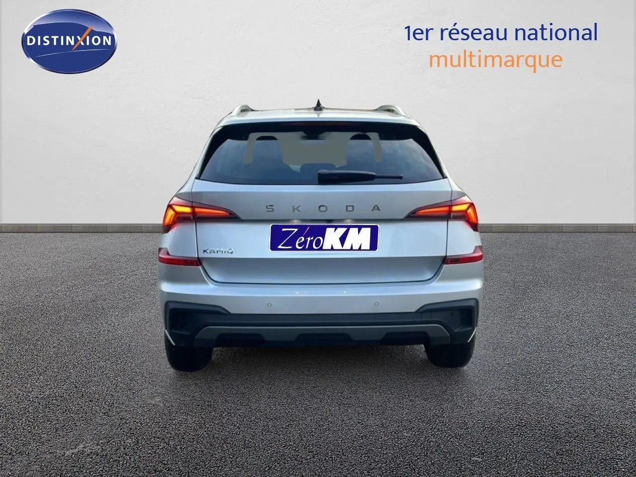 Vue arrière d'un Skoda Kamiq gris argent métal 2025 avec feux allumés et plaque Zéro KM visible.
