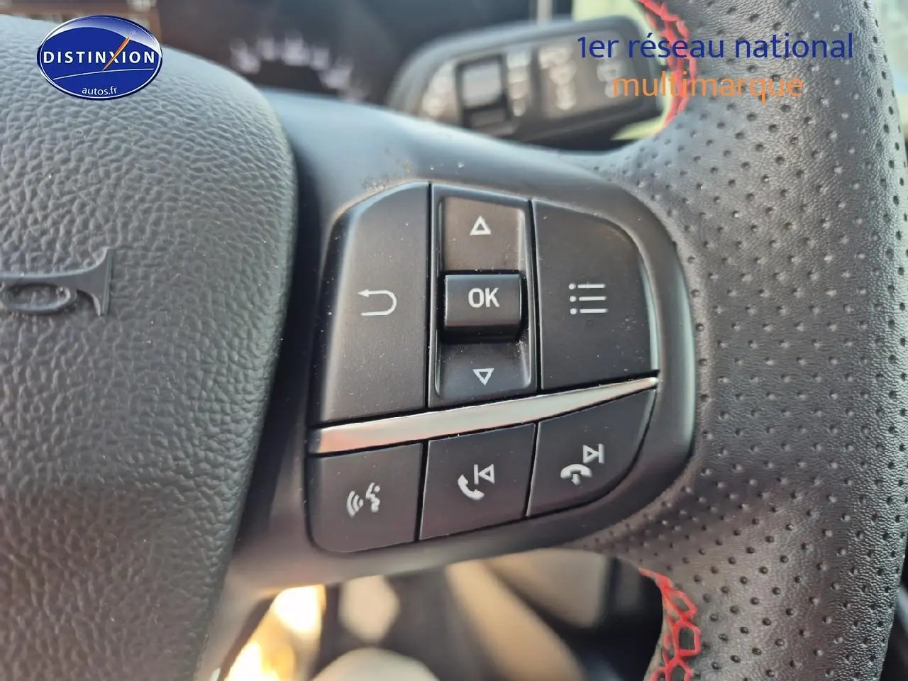 Gros plan sur les commandes multifonctions du volant cuir perforé avec surpiqûres rouges d'une Ford Focus gris magnétique.