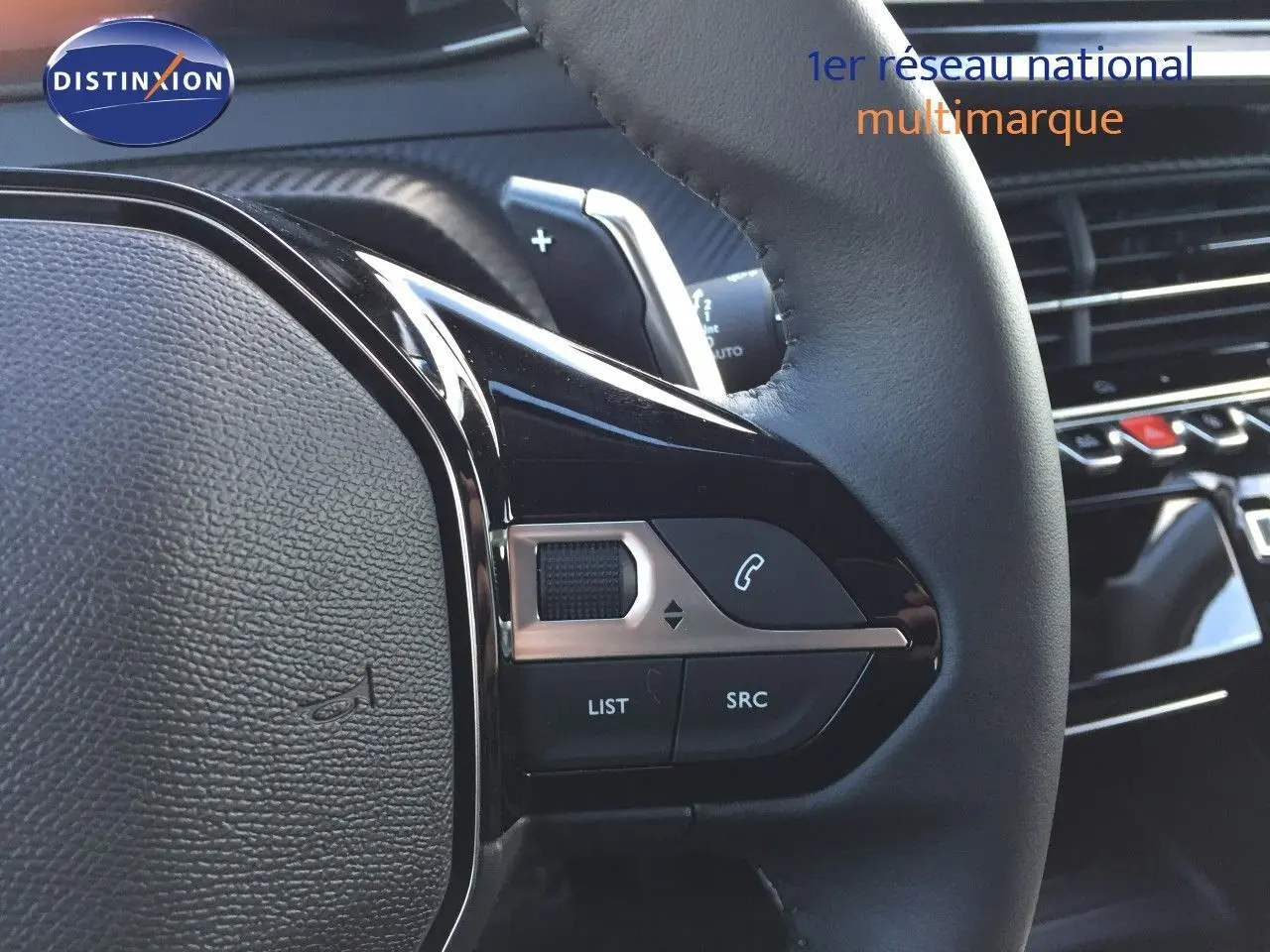 Gros plan sur les commandes au volant en cuir noir de la Peugeot 208 1.2 Hybrid 2025, intérieur moderne et soigné.