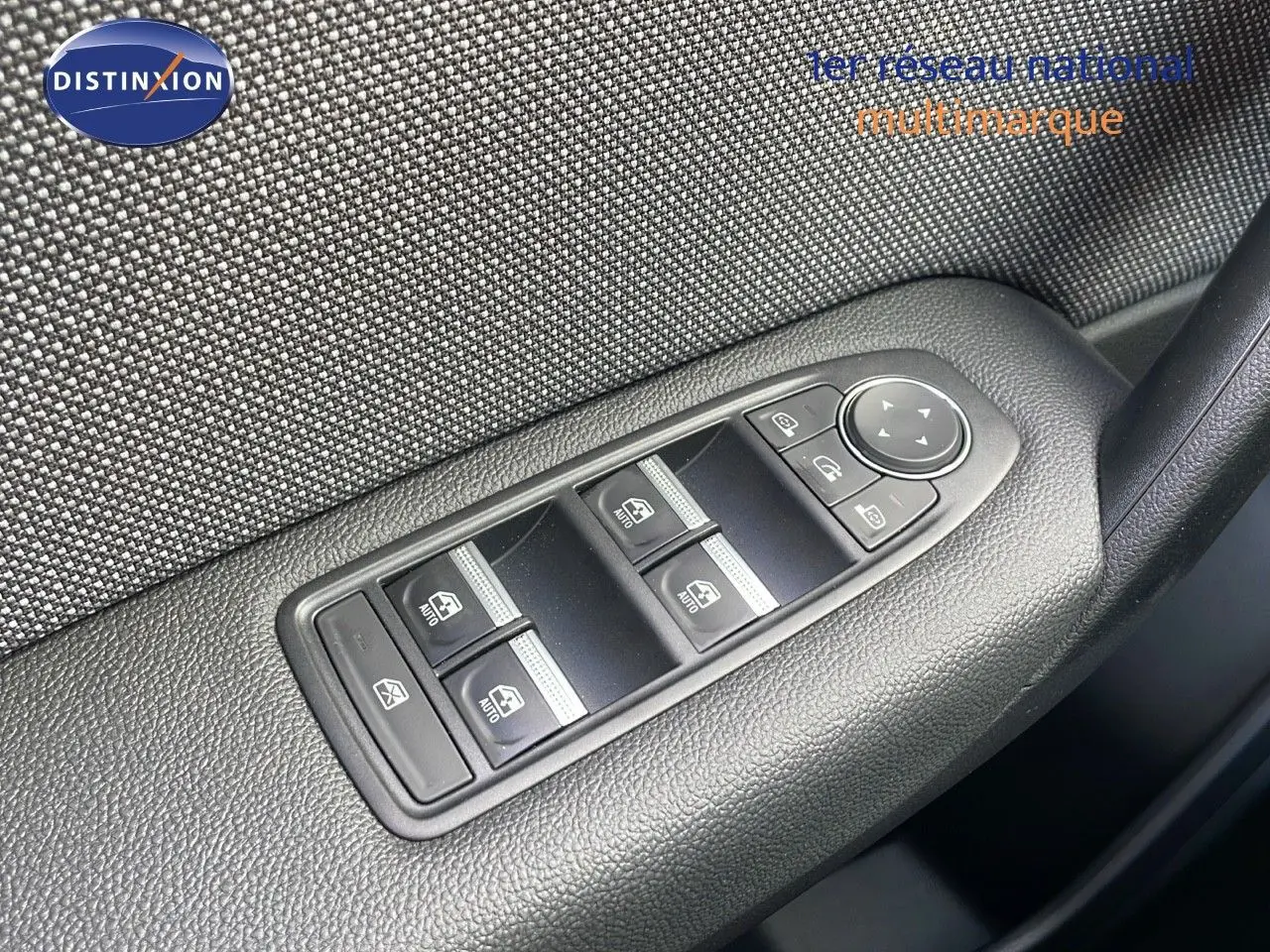 Panneau de commandes des vitres électriques côté conducteur sur porte intérieure en tissu gris et plastique noir.