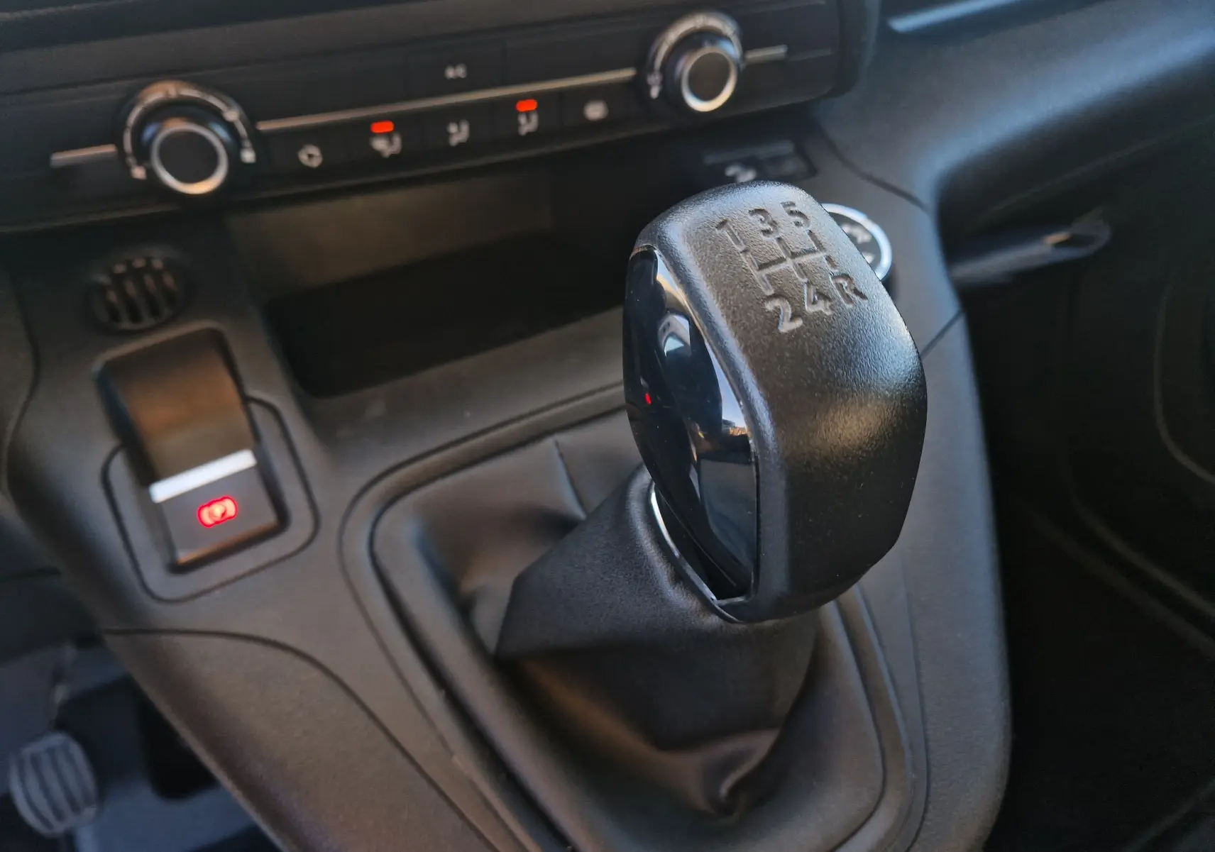 Gros plan sur le levier de vitesses manuel noir du Peugeot Partner blanc, avec commandes de climatisation en arrière-plan.