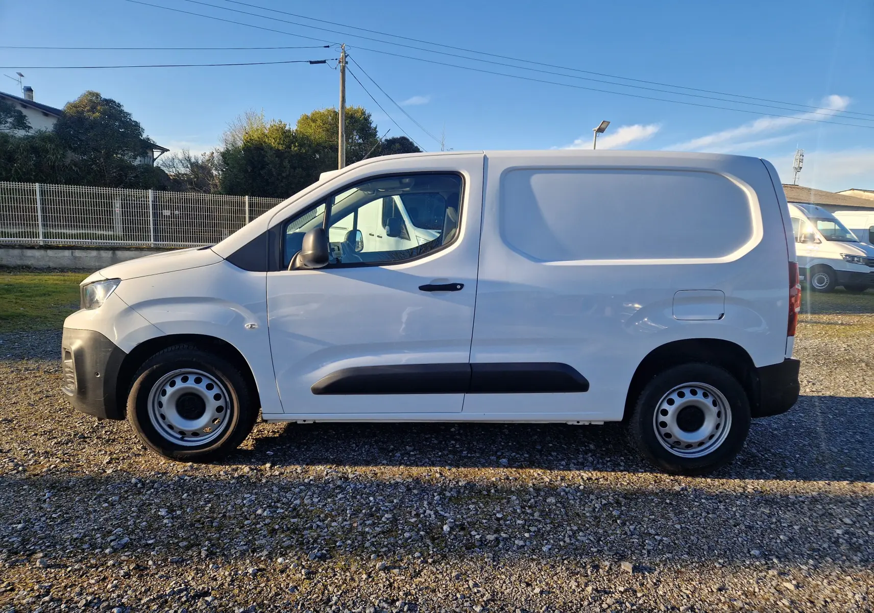 Vue de profil côté gauche d’un utilitaire Peugeot Partner blanc 2021 avec porte latérale pleine et jantes acier.