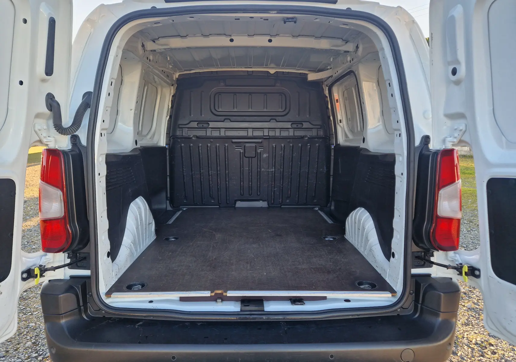 Vue arrière ouverte du Peugeot Partner blanc 2021, montrant l'espace de chargement vide avec plancher en bois et parois noires.