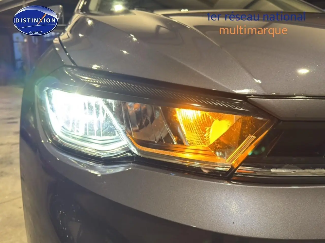 Gros plan sur le phare avant gauche allumé d'une Volkswagen Polo gris cendre, avec clignotant orange visible.
