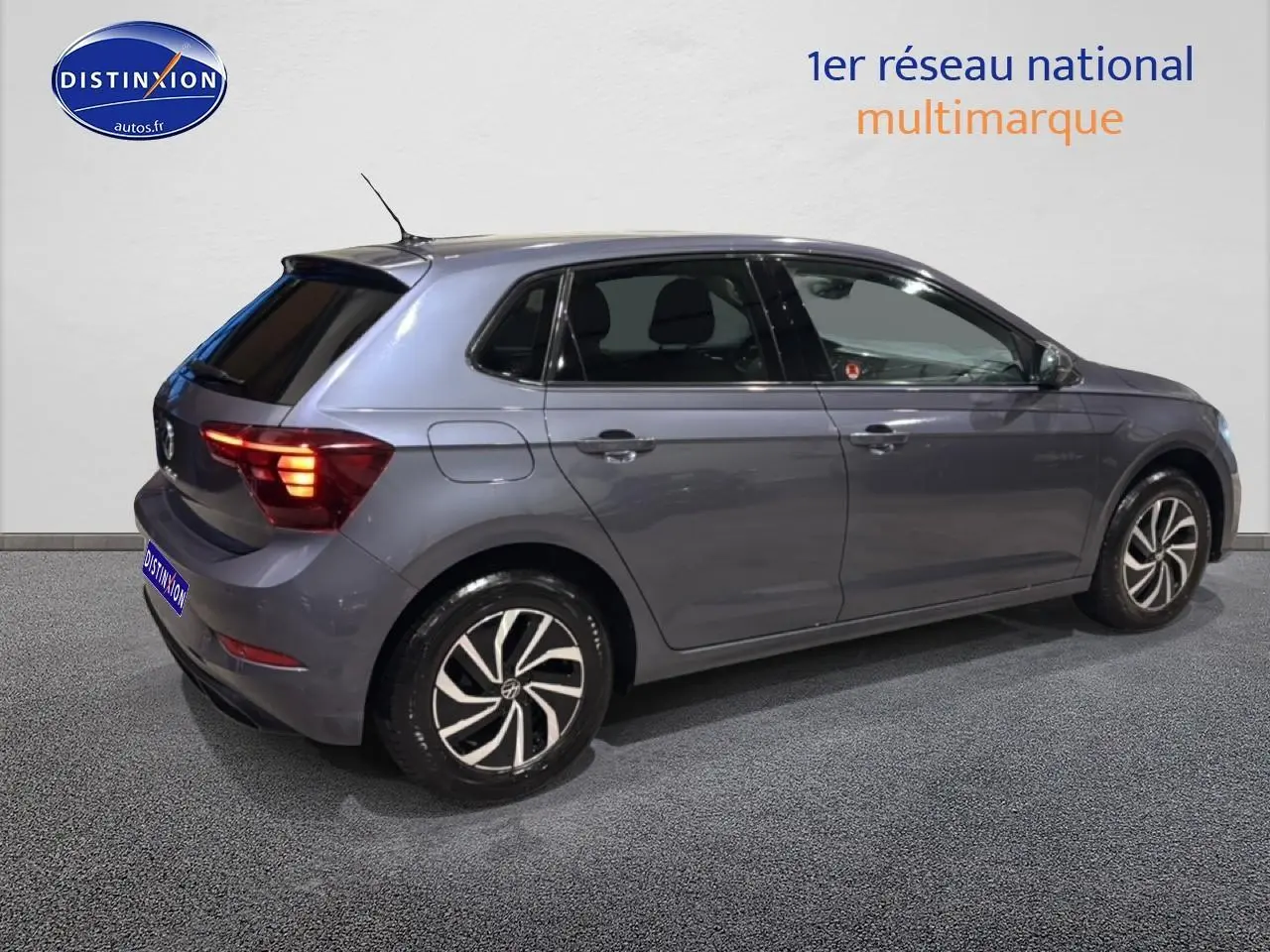 Volkswagen Polo gris cendre vue de profil côté droit avec feux arrière allumés en intérieur showroom.