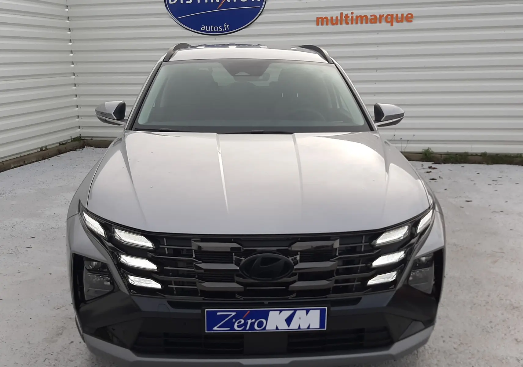 Vue frontale d'un Hyundai Tucson gris Shimmering Silver 2025 avec calandre noire et feux LED allumés.