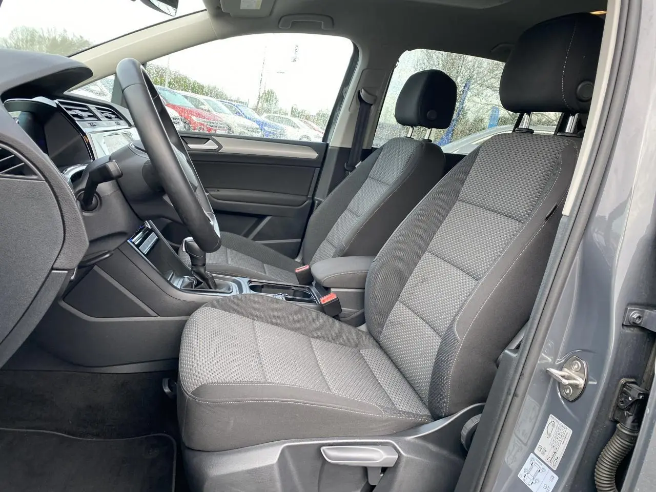 Vue intérieure côté conducteur du Volkswagen Touran gris dauphin, montrant les sièges avant et le volant multifonction.