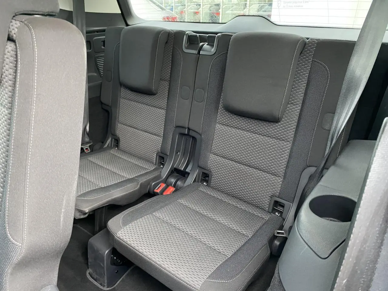 Vue intérieure sur les sièges arrière gris foncé du Volkswagen Touran 2025, avec accoudoir et porte-gobelet intégrés.