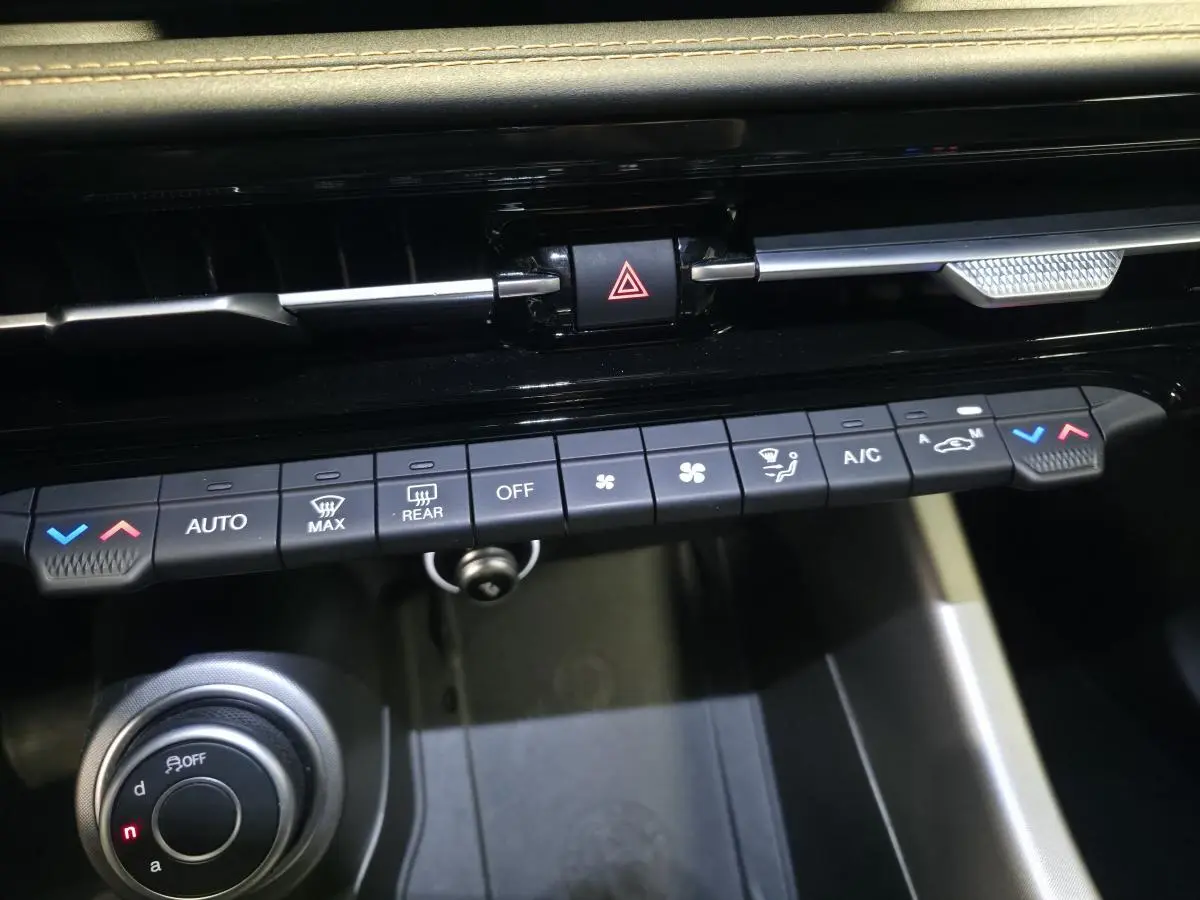 Gros plan sur la console centrale de l'Alfa Romeo Tonale gris, montrant les commandes de climatisation et le bouton de sélection de mode de conduite.