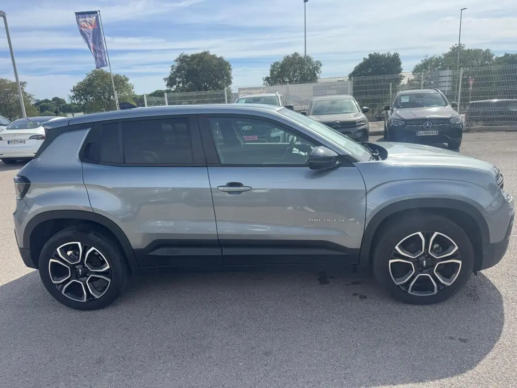 Vue de profil côté gauche d’un Jeep Avenger gris foncé 2025 avec jantes distinctives et toit noir contrasté.