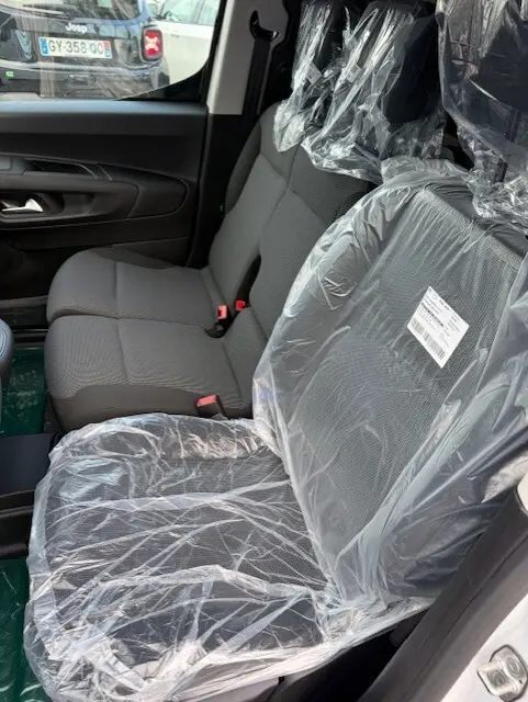 Vue intérieure côté droit du Citroën Berlingo 2026, sièges avant en tissu gris protégés par des housses plastiques.